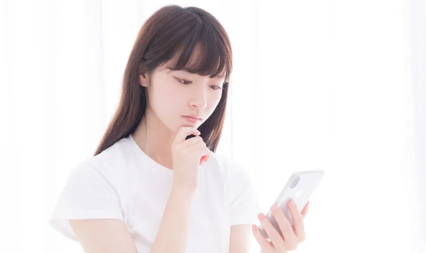 スマートフォンを見つめて考え込む女性