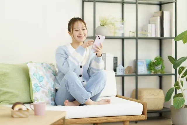 ソファに座ってスマホを片手に喜ぶ女性