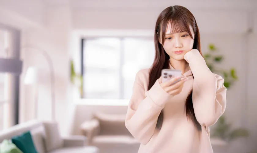 スマートフォンを持って考えこむ女性