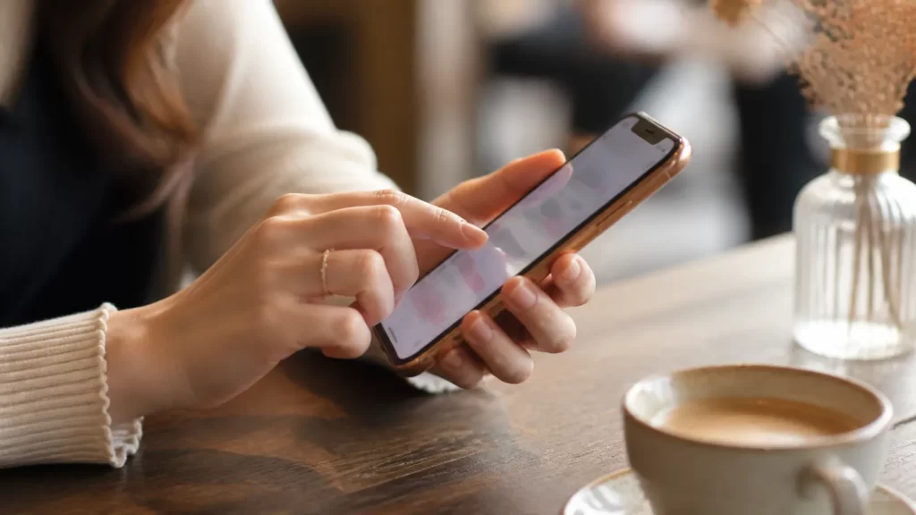 カフェのテーブルでスマートフォンに丁寧にメッセージを打つ女性の手元のアップ。