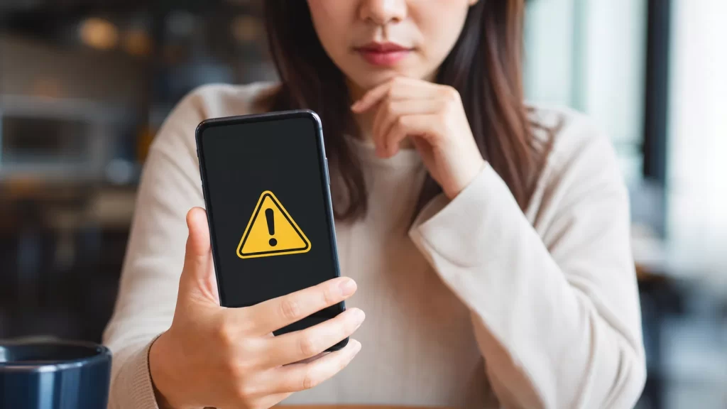 スマートフォンの画面に表示された警告アイコンと、女性の真剣な表情の手元