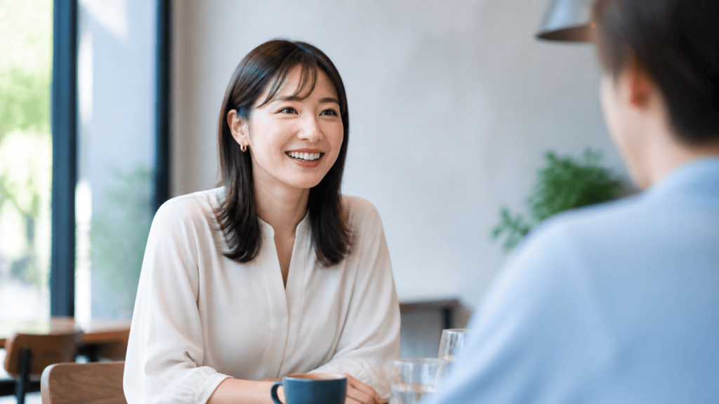明るいカフェで上品な装いの成人女性が笑顔で会話する、清潔感のある編集写真。