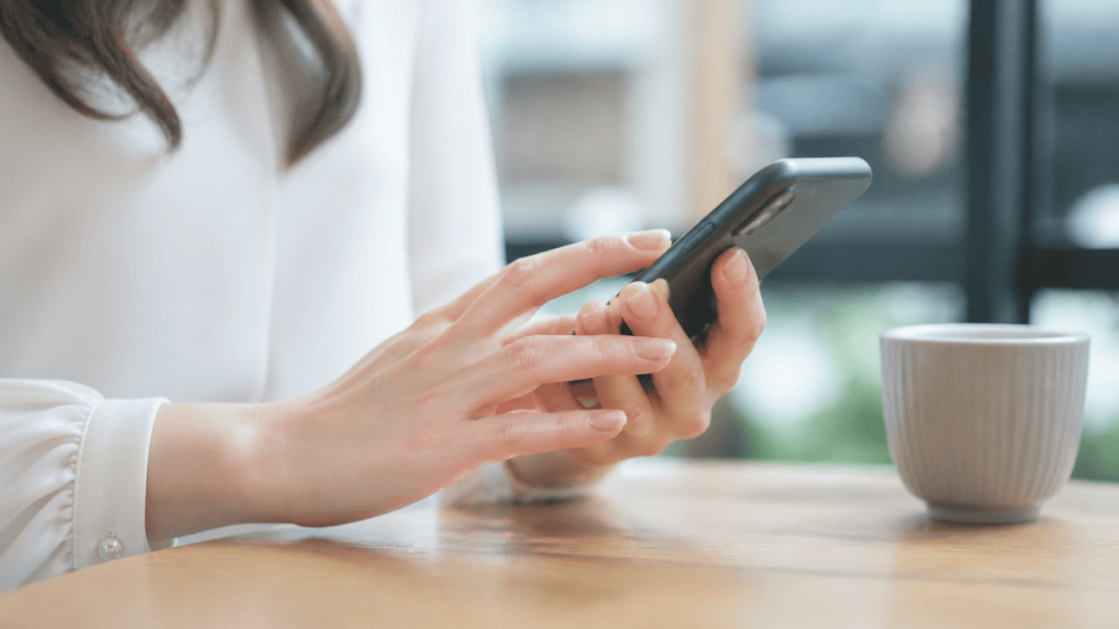 成人女性がスマートフォンで丁寧にメッセージを打つ手元。画面は読めない構図。