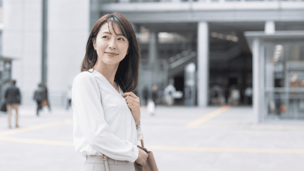 明るい駅前で時間より早く到着し、穏やかに待つ成人女性。