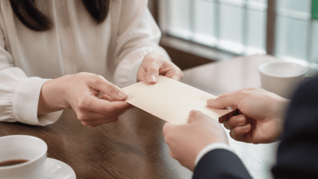 無地の封筒を両手で丁寧に受け取る成人同士の手元。現金や文字は見せない。