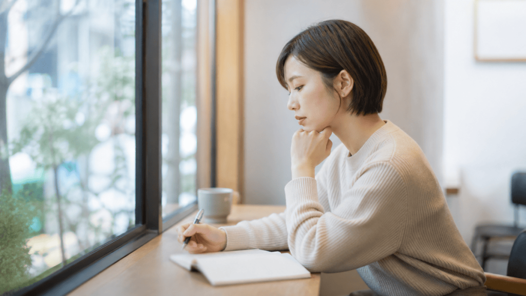 パパ活の体験を振り返りながらノートを書く成人女性